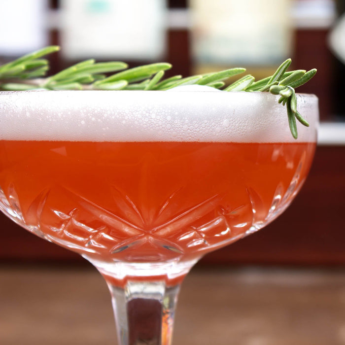 Cocktail with foam and rosemary garnish in a decorative glass.