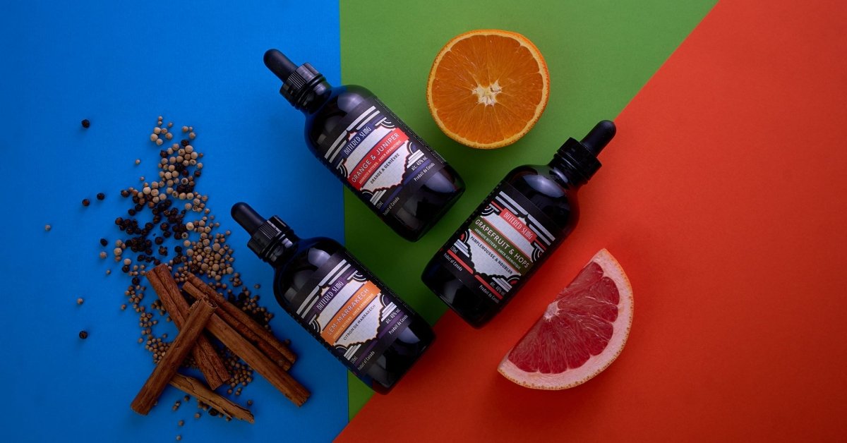 Three black dropper bottles on a colorful background with spices and fruit slices.