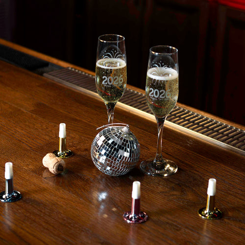 Two champagne glasses with '2023' on a wooden surface with candles and a disco ball.