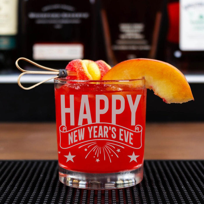Red glass with 'Happy New Year's Eve' text, garnished with peach slices and a straw, on a bar counter.