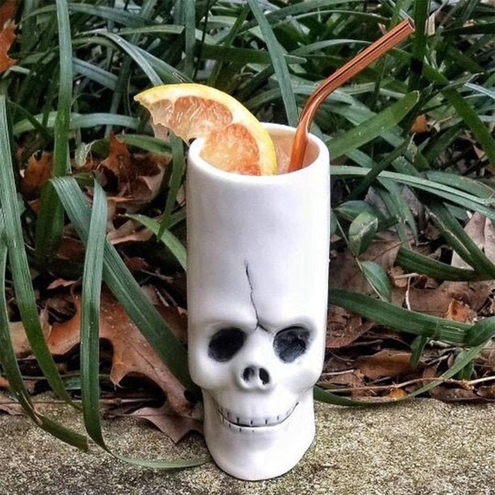 Skull-shaped cup with a drink and orange slices on a grassy background