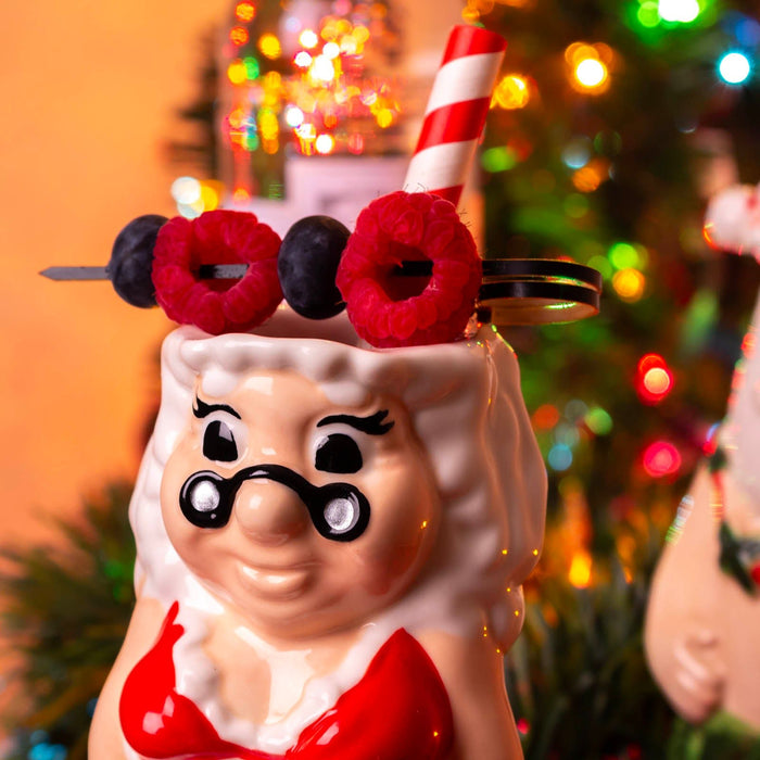 Decorative figure of ms. claus with a Santa hat, berries, and a candy cane against a festive background.