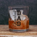A clear rocks glass with black 'Baseball DAD' lettering, filled with an amber drink and large ice cubes, set on a wooden surface against a dark textured background.