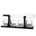 A whiskey decanter set with a clear glass bottle resting horizontally on a black metal stand, with four matching clear glass tumblers on the base, photographed on a white background.
