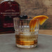 Glass of whiskey with orange slice and cherries in front of Woodford Reserve bottle