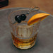 Glass of whiskey with cherries and an orange wedge on a gray surface