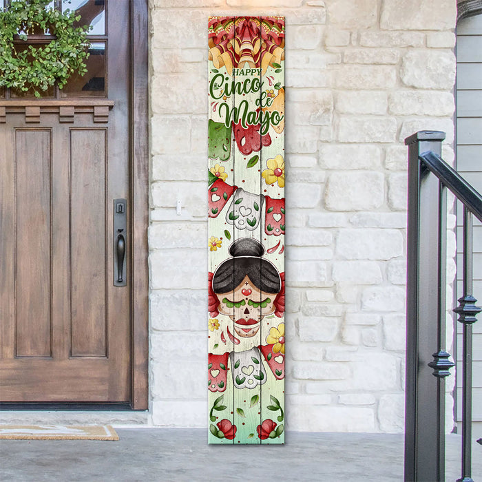 Decorative sign with 'Happy Cinco de Mayo' text on a vertical board against a stone wall.