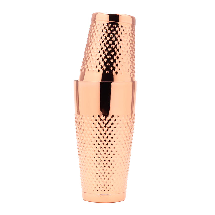 A polished copper cocktail shaker with a textured, diamond-patterned grip, shown stacked with two matching tumblers on a solid white background.
