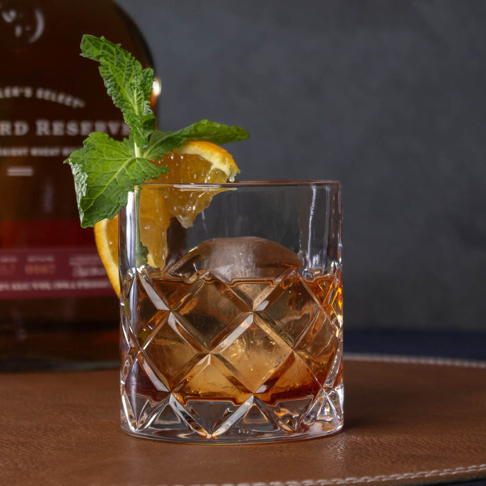 Glass of whiskey with ice and garnish in front of a bottle of woodfrod reserve.