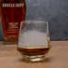 Glass of whiskey with ice cubes next to a bottle of Angels Envy bourbon.