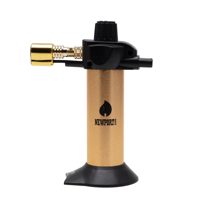 A portable torch lighter with a brushed gold body, black nozzle and base, and a brass connector on the side, featuring the Newport brand logo on the front.