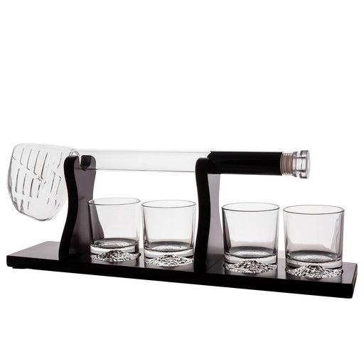 A clear glass decanter with a black handle and four matching clear glass tumblers on a black base, with a clear slotted scoop or spoon resting on the left side, photographed on a white background.