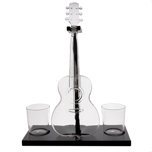 A clear glass acoustic guitar-shaped decanter with a black base, shown on a white background with two small clear glasses on either side of the base.