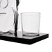 A clear glass tumbler cup sitting on a black rectangular base, with part of a transparent glass carafe visible at the left edge against a white background.