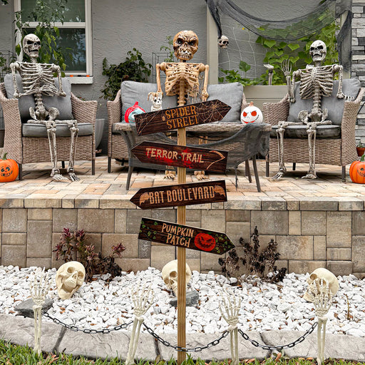 Halloween outdoor scene with skeletons, pumpkins, and a signpost on a patio.