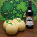 Bottle of Irish Cream Cordial Syrup with creamy drinks and shamrock decorations on a St. Patrick's Day-themed background.