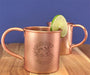 Copper Moscow Mule mugs with lime slices on a wooden surface against a blue background