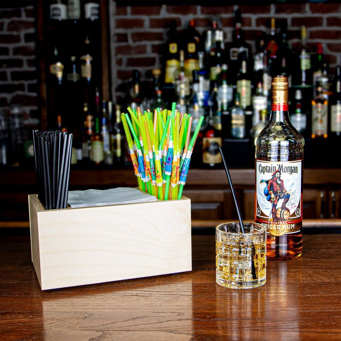 Bar setup with bottle, glass, and wooden natural napkin caddy on a bar top surface. 