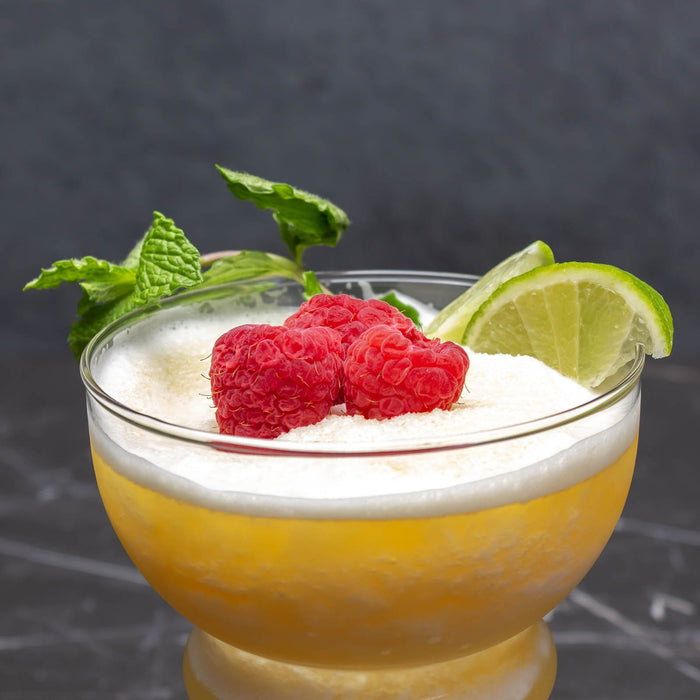 Glass of yellow drink with raspberries and lime on a dark background