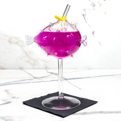 Purple cocktail in a fish-shaped glass with a straw on a marble surface