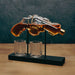 A clear glass revolver-shaped decanter filled with amber liquid, mounted on a black stand with two clear glasses below, set on a wooden surface against a dark textured background.