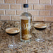 Bottle with custom label with two glasses of a dark beverage on a countertop.