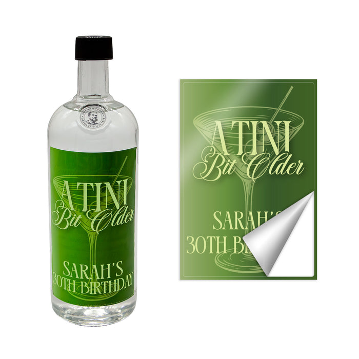 Bottle with a customizable 'A Tini Bit Older' green label and a matching sticker on a white background