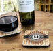 Wine bottle and glass on a wooden table with a coaster featuring a monogram 'M'.